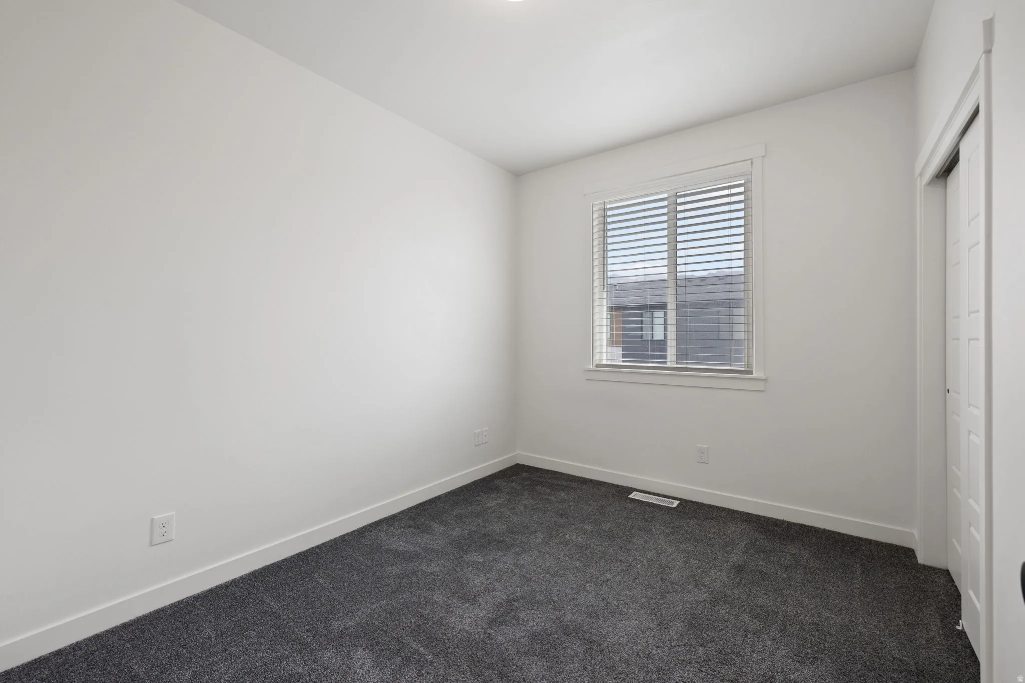 Room featuring soft gray carpeting, white walls, and a window with horizontal blinds