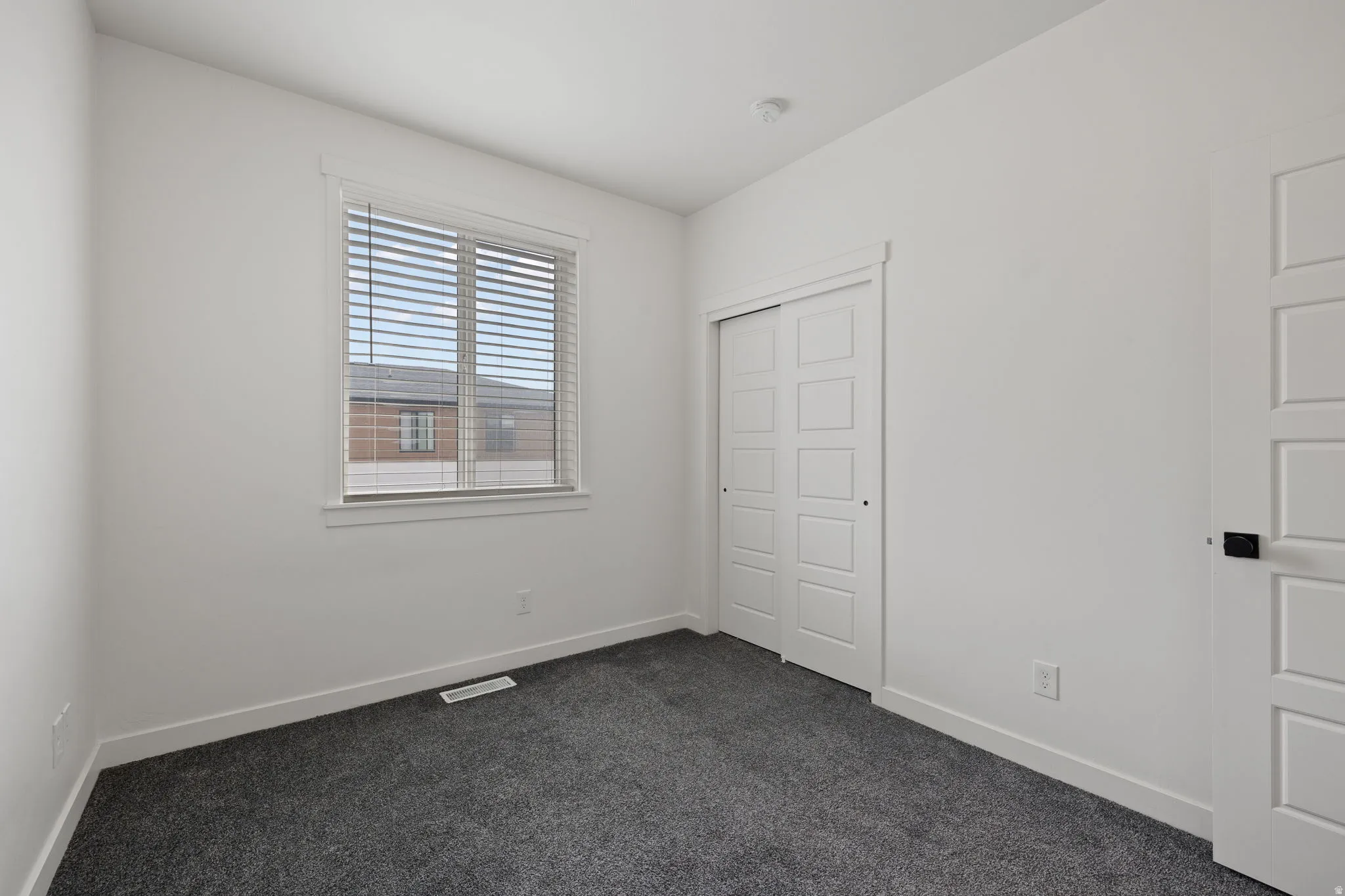 Room featuring neutral-toned walls, dark gray carpeting, and a window with horizontal blinds