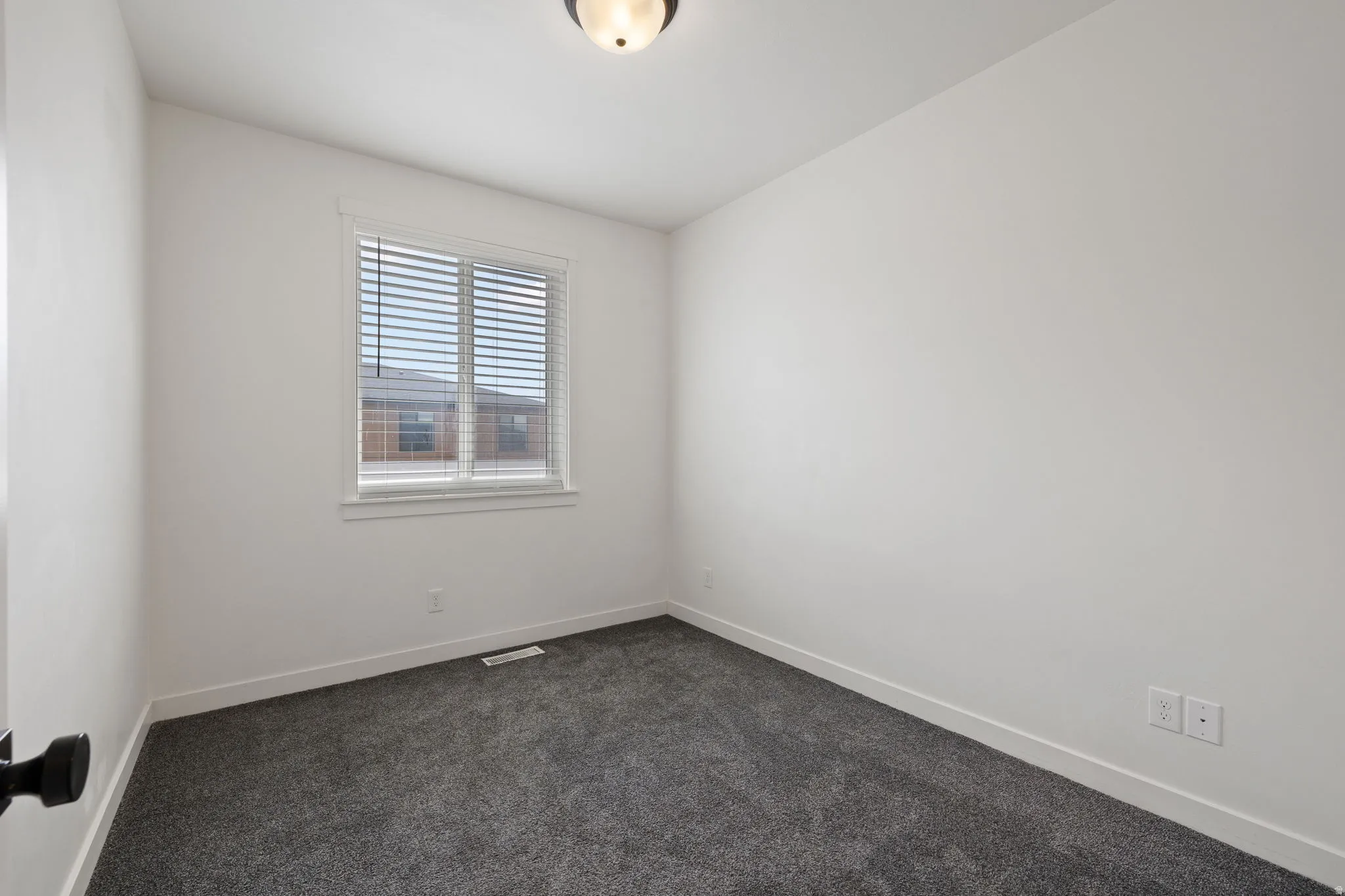 Interior space featuring a single window with blinds, neutral wall paint, ceiling-mounted light fixture, and textured gray carpeting