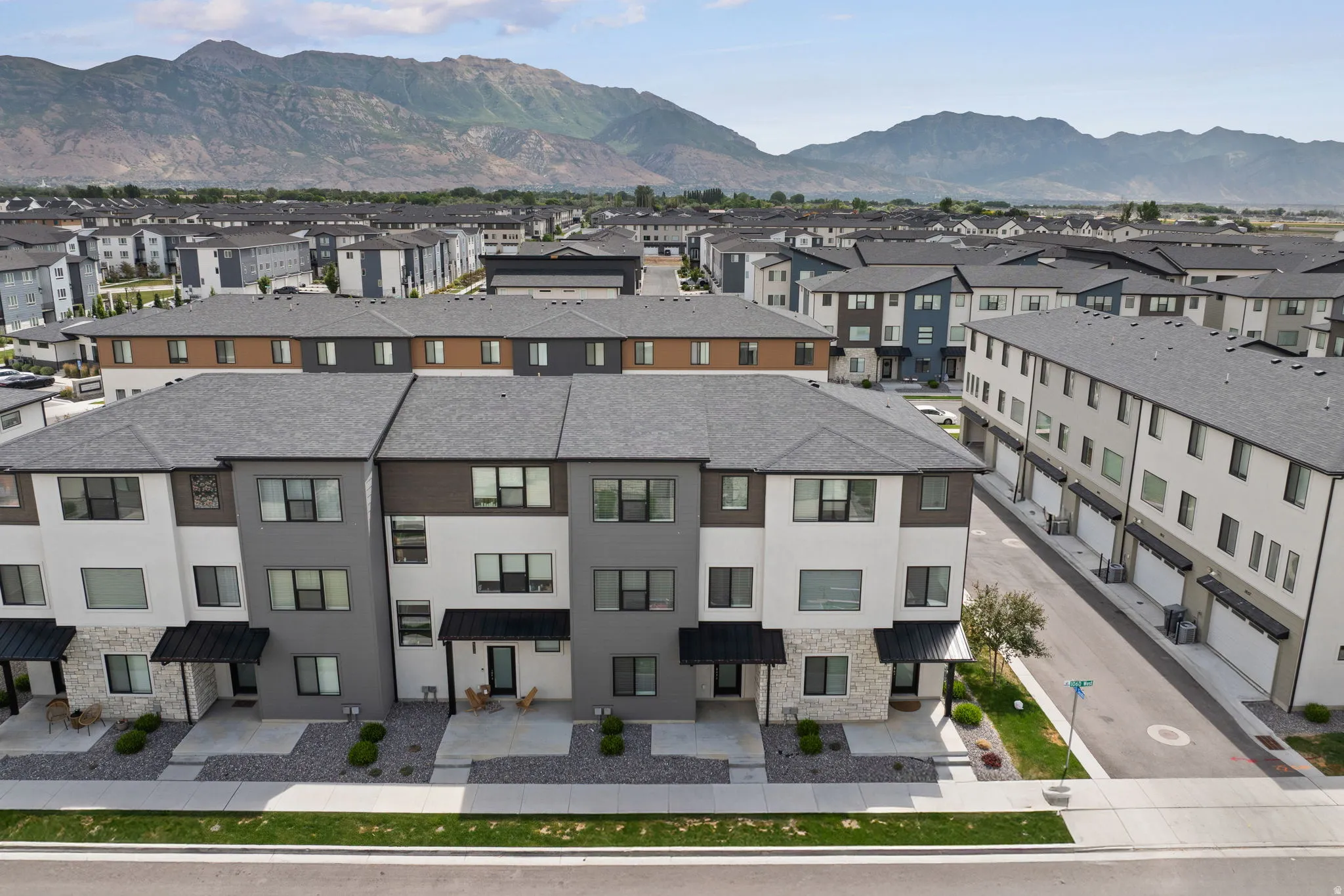Contemporary townhome exterior featuring a stone and siding facade, black metal awnings, and a gravel front yard