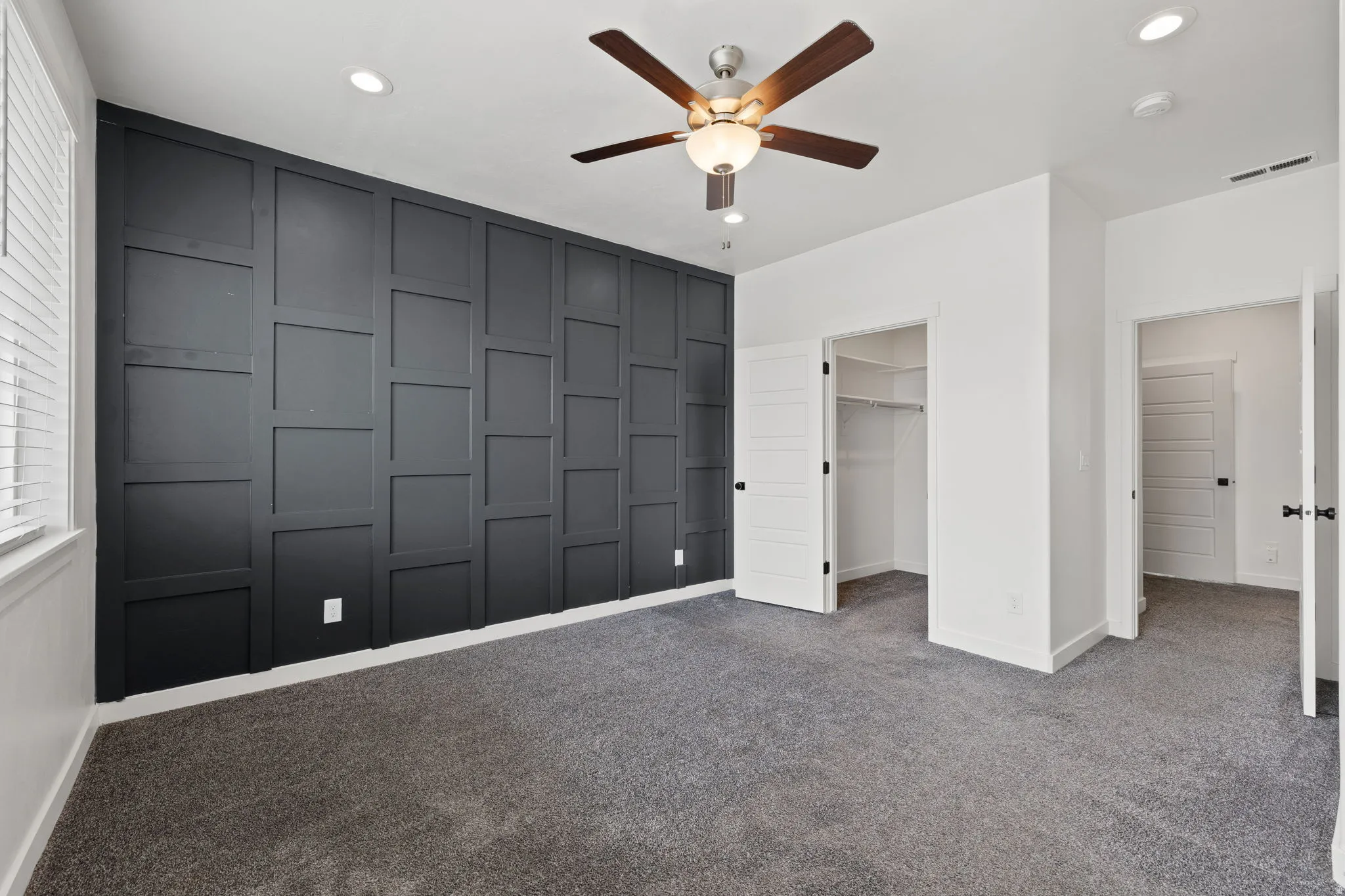 Feature wall with dark paneling, recessed lighting, ceiling fan with wood-finish blades, gray carpet flooring, and white trim