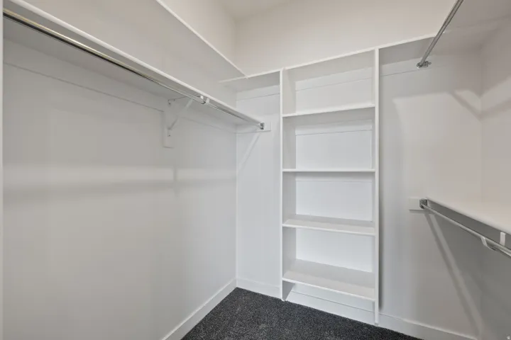 Walk-in closet featuring white walls, dark carpet flooring, and built-in white shelving
