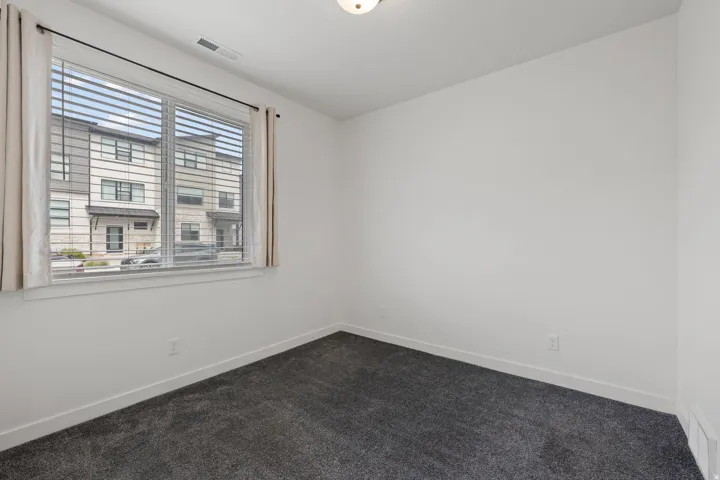 Bright interior space featuring a large window with blinds and curtains, neutral wall paint, and dark gray carpeting