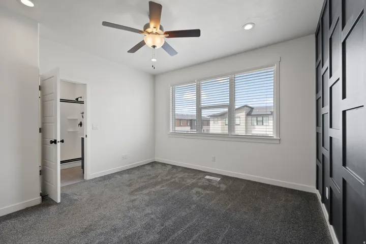 Spacious room featuring gray carpeting, a multi-pane window with blinds, and a dark accent wall with geometric paneling