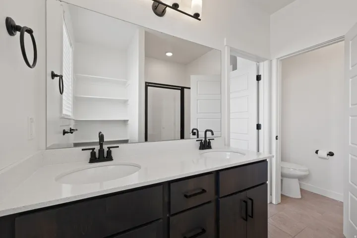 Dual undermount sinks set in a white countertop, dark wood-finish cabinetry with matte black hardware, and a large wall-mounted mirror