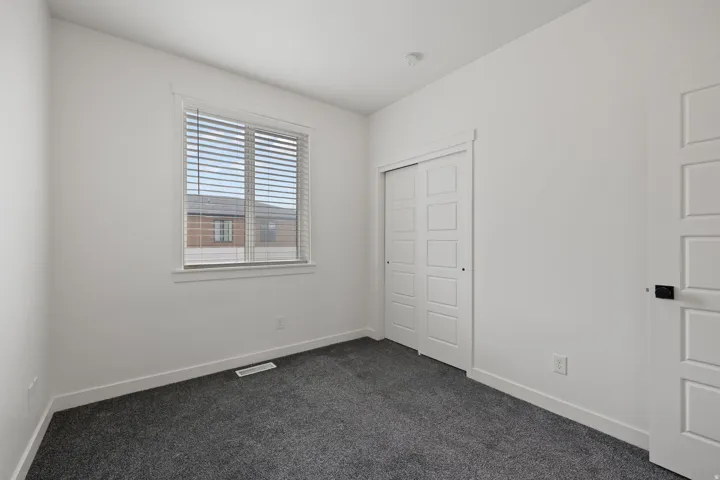 Room featuring neutral-toned walls, dark gray carpeting, and a window with horizontal blinds
