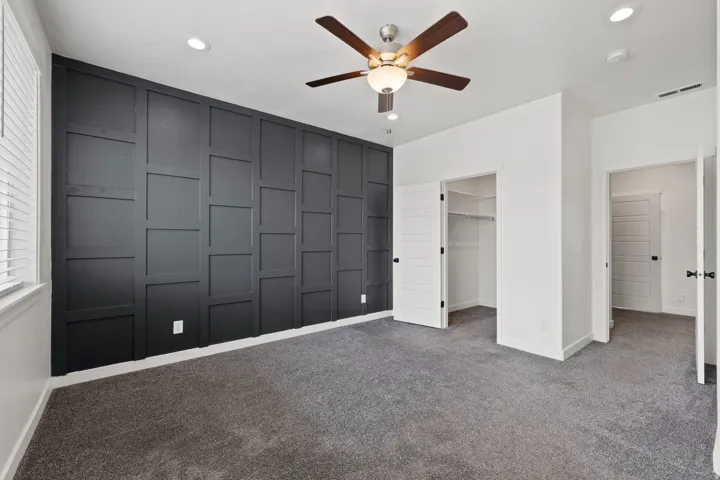 Feature wall with dark paneling, recessed lighting, ceiling fan with wood-finish blades, gray carpet flooring, and white trim