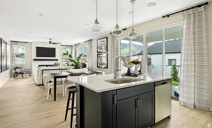 Open-concept living space featuring a kitchen island with a built-in sink and stainless steel dishwasher, wood-finish flooring, recessed lighting, and large sliding glass doors leading to outdoor space