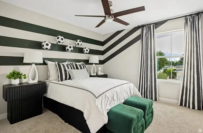 Carpeted room featuring a ceiling fan with light fixture, large window with ample natural light, and distinctive striped wall accents