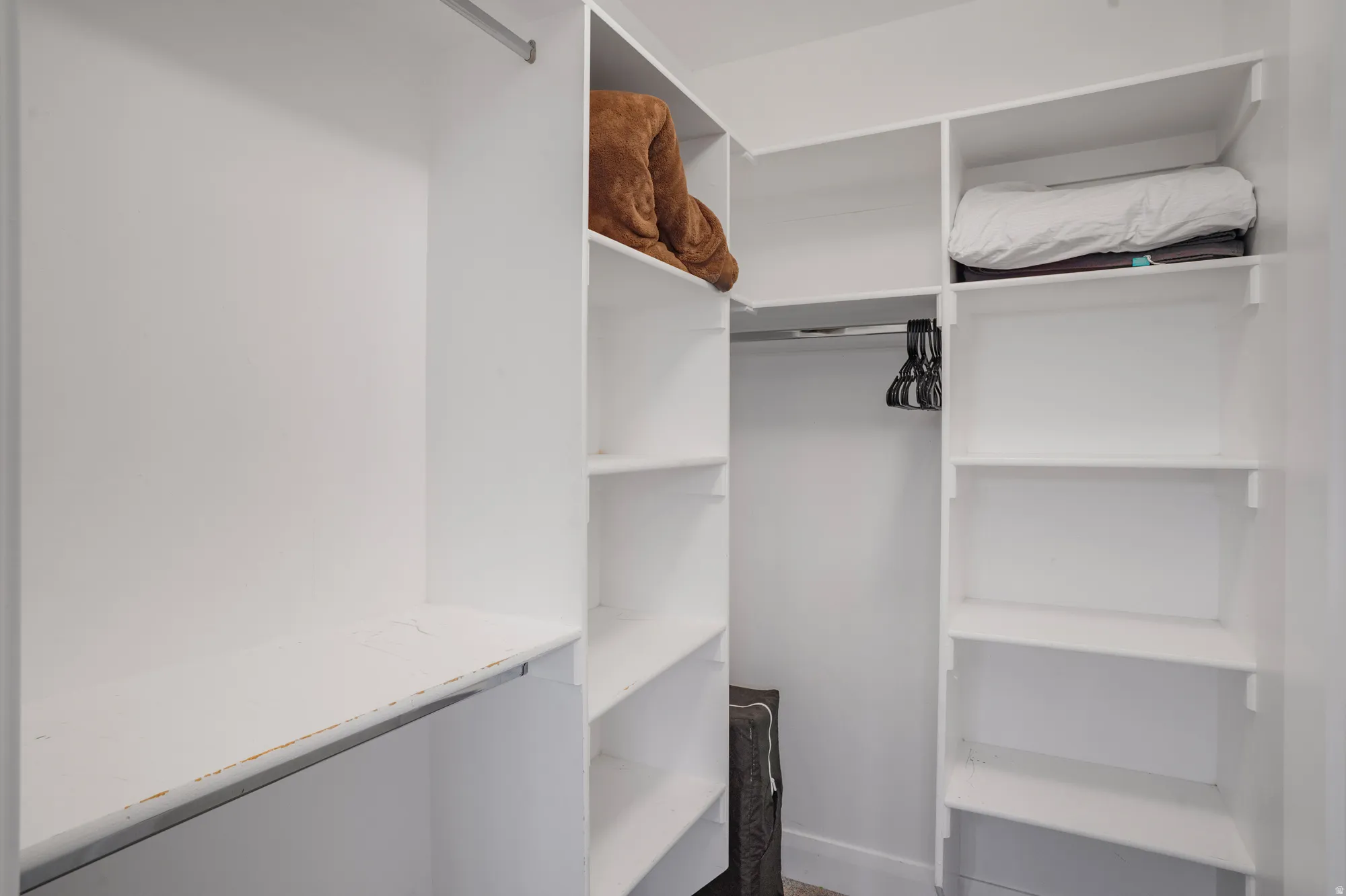 Walk-in closet featuring white built-in shelving, multiple hanging rods, and a neutral wall finish