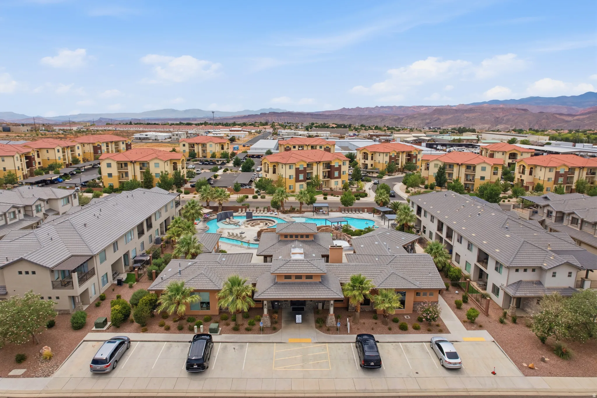 Expansive community featuring multiple residential buildings with tile roofs, a central clubhouse, and a resort-style swimming pool area with integrated spa