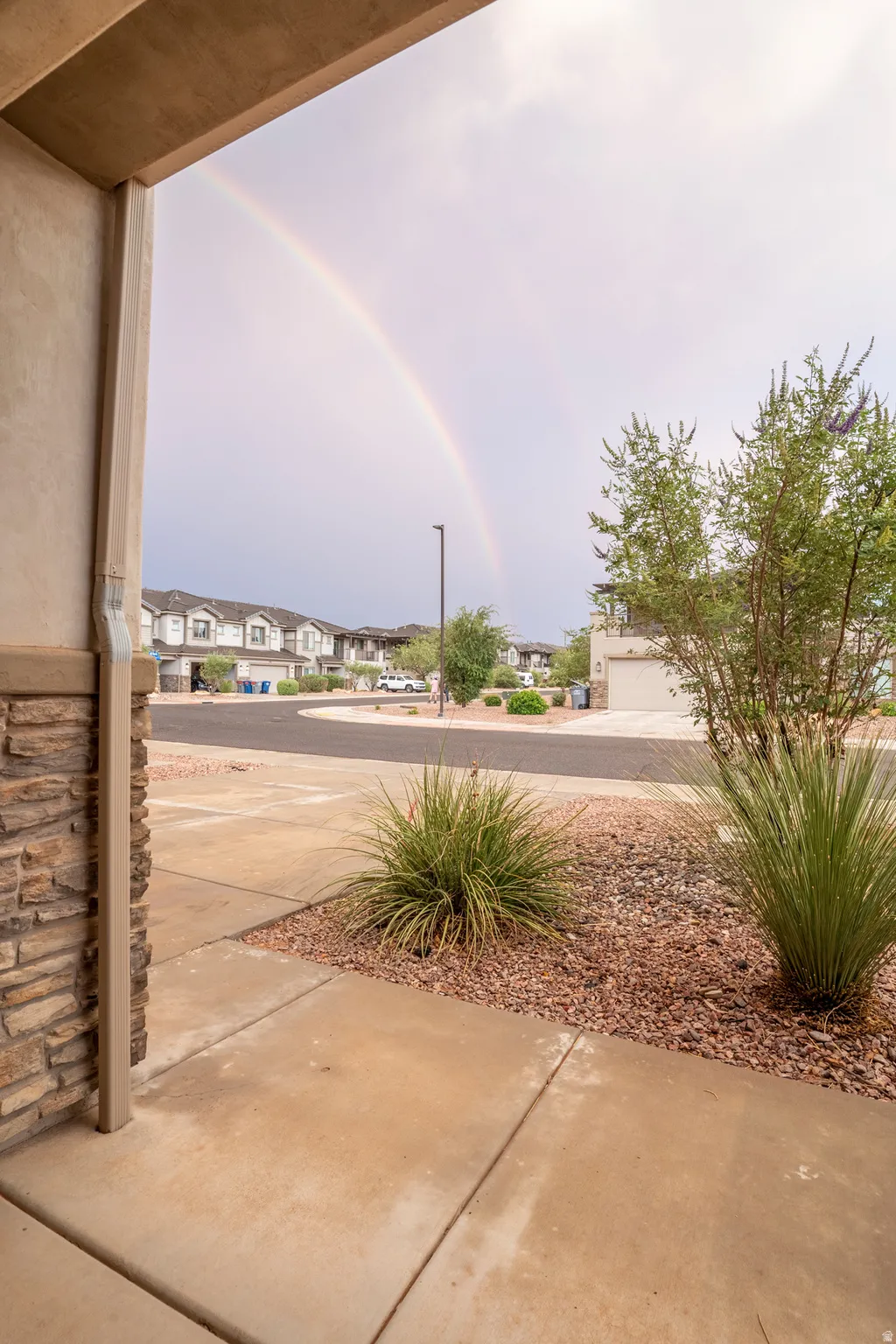 Stucco and stone facade entrance featuring concrete walkway, low-maintenance landscaping with decorative rock, and mature plantings