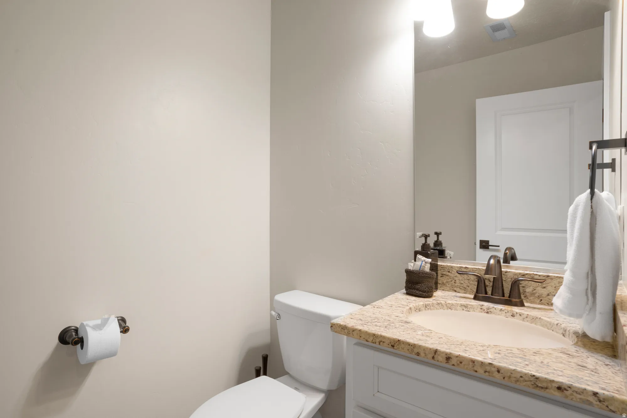 Bathroom vanity featuring a light granite countertop with an undermount sink, bronze-finish faucet, and coordinating mirror