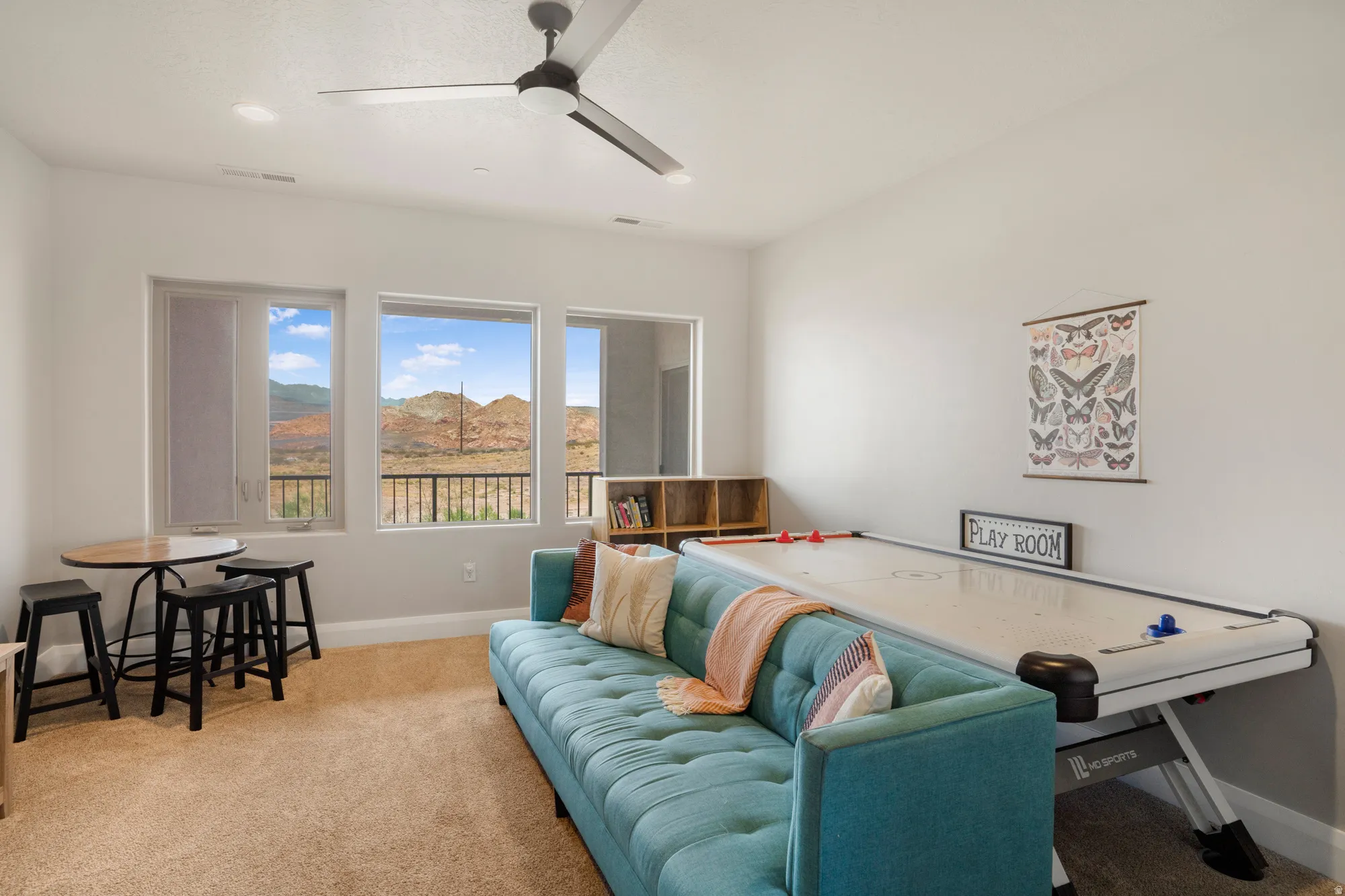 Bright living space featuring multiple windows, mountain scenery, carpeting, built-in shelving, and a ceiling fan