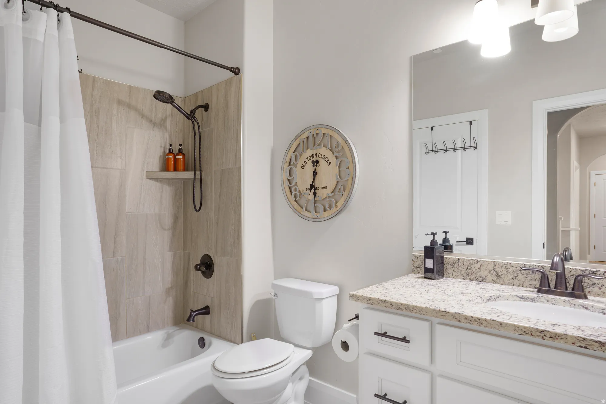 Full bathroom featuring a tub/shower combination with tile surround and integrated shelving, oil-rubbed bronze fixtures, a vanity with a granite-style countertop, and ample cabinet storage