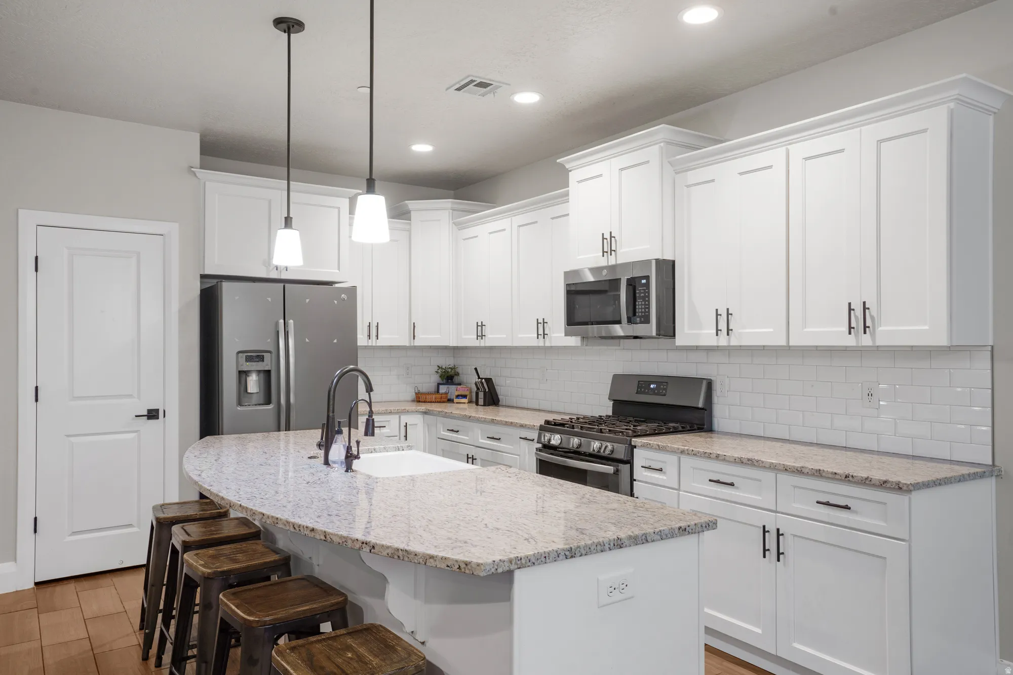 Contemporary kitchen featuring white shaker cabinetry, stainless steel appliances, a subway tile backsplash, granite countertops, and recessed lighting
