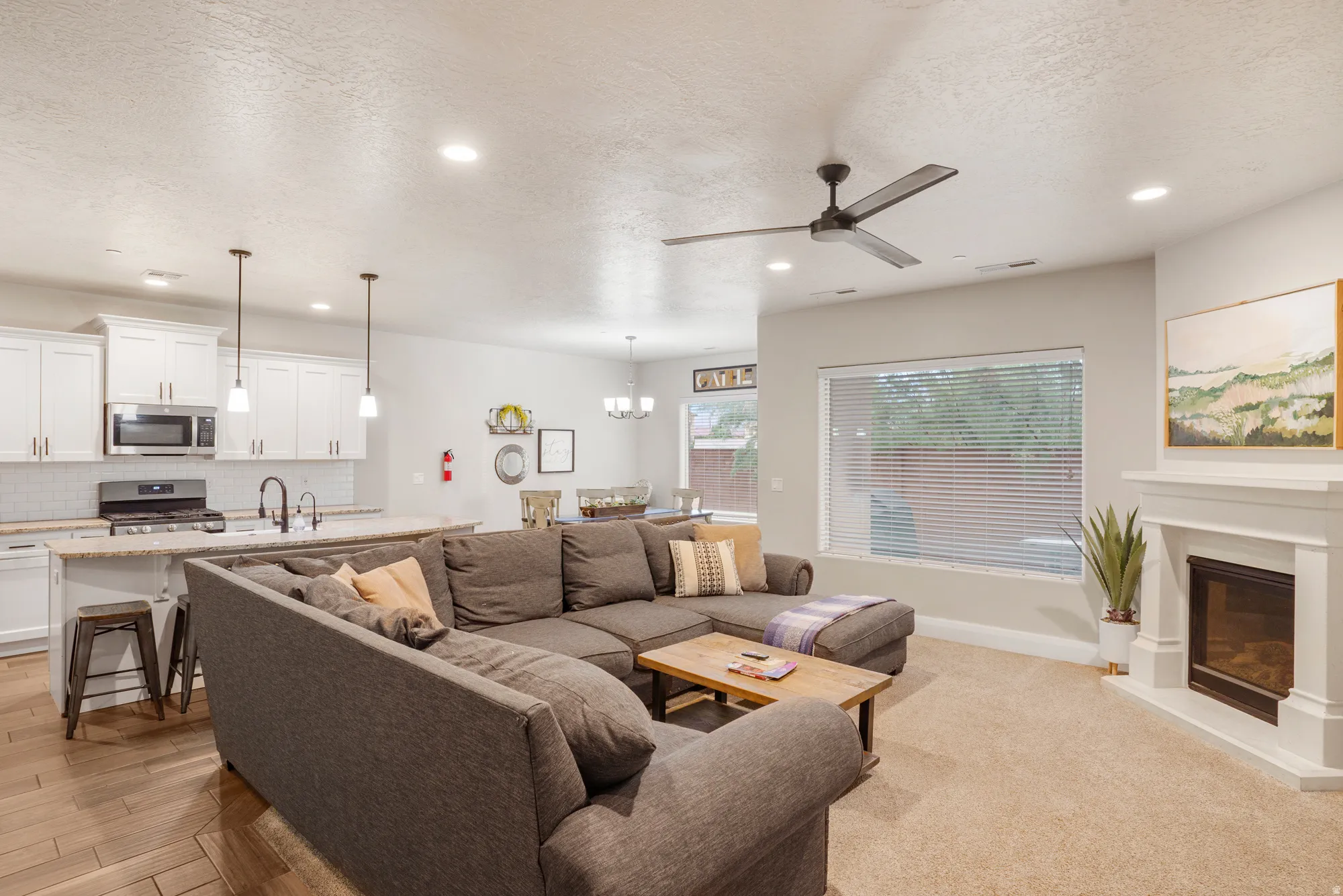 Open-concept living area featuring wood-finish flooring, a contemporary fireplace with a white mantel, and a ceiling fan with integrated lighting