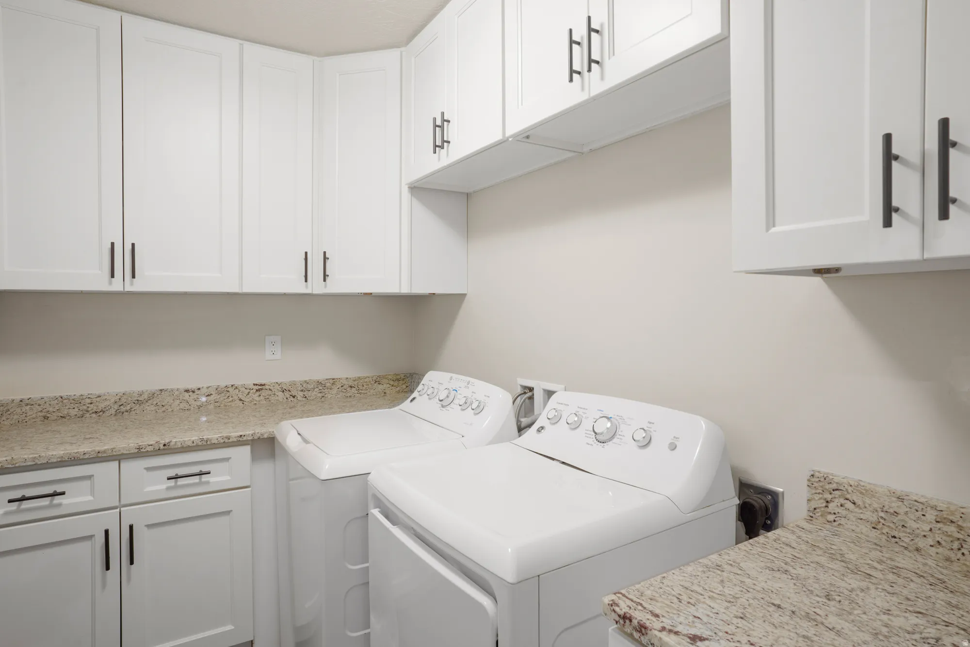 Laundry area featuring white shaker-style cabinetry with matte black hardware, granite-look countertops, and ample storage