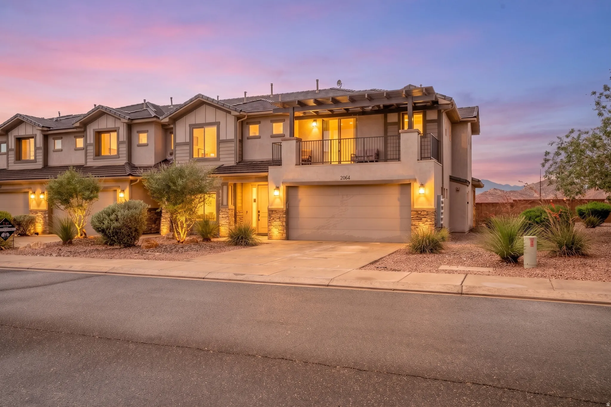 Stucco exterior with stone accents, a private balcony featuring a pergola, and an integrated garage