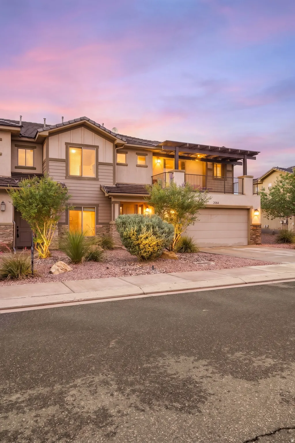 Multi-story exterior with a two-car garage, stone accents, and an upper-level balcony featuring a pergola