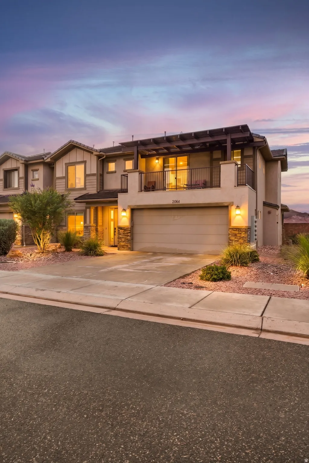 Multi-level townhome with stone accents, an attached two-car garage, and a private balcony featuring a pergola