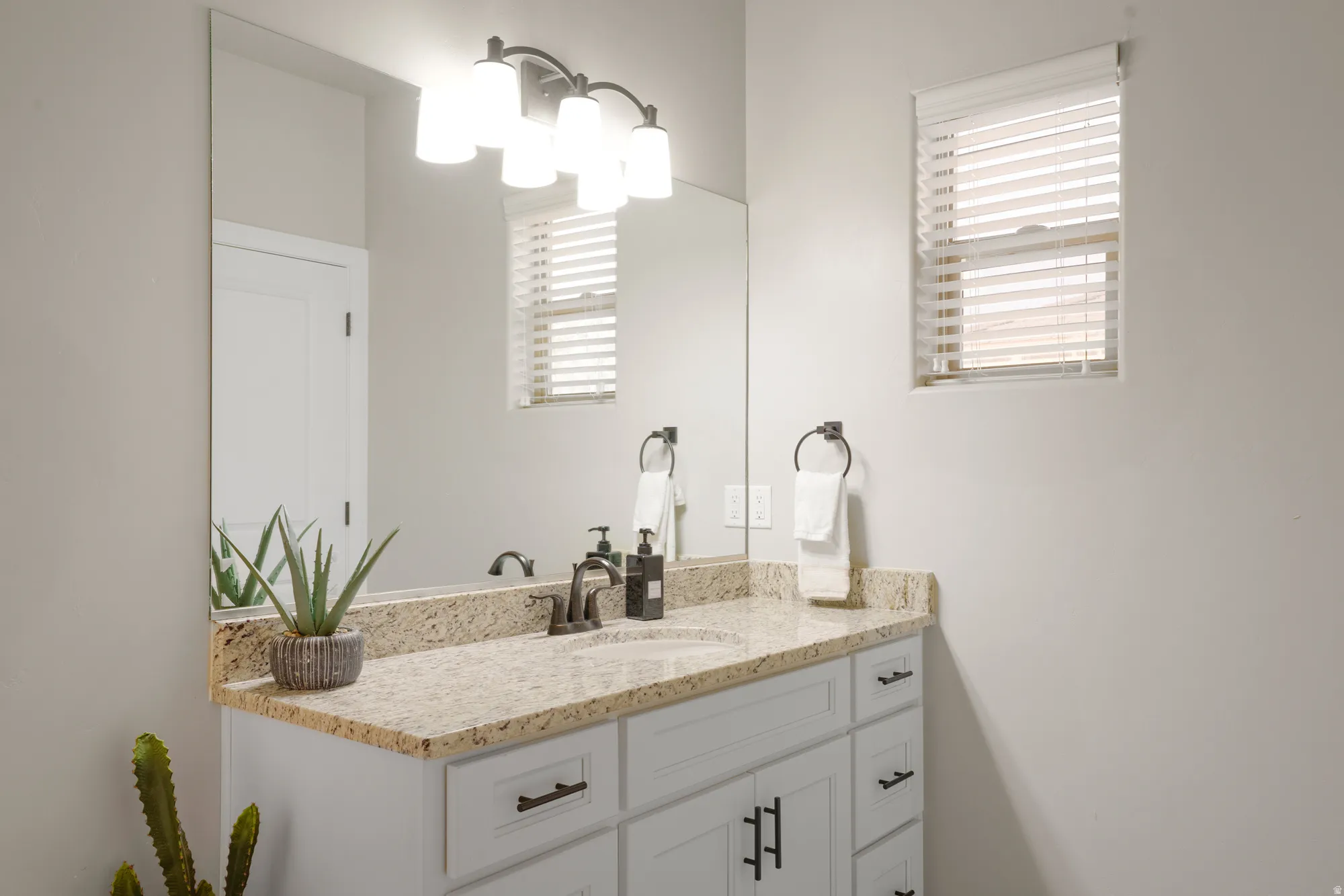 Bathroom vanity featuring a light-toned countertop, white cabinetry with dark hardware, an undermount sink, and a wall-mounted mirror