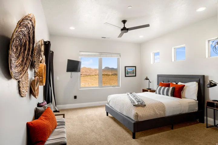Carpeted bedroom featuring a large window with desert scenery, recessed lighting, a ceiling fan, and multiple high windows