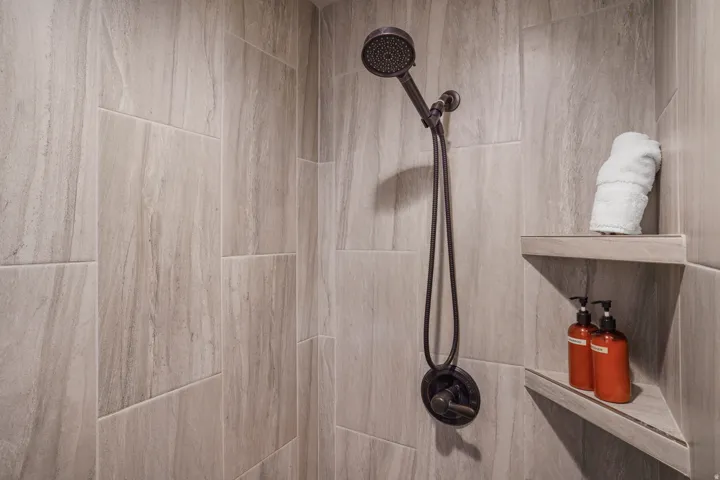 Shower with large format stone-look tile, dark bronze showerhead, and integrated corner shelving