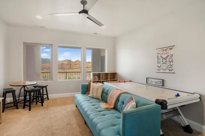 Bright living space featuring multiple windows, mountain scenery, carpeting, built-in shelving, and a ceiling fan