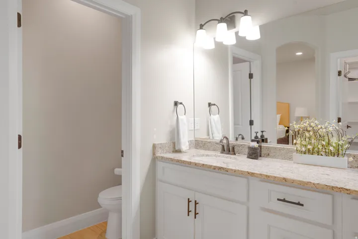 Bathroom vanity featuring a light granite countertop with an undermount sink, white cabinetry with dark hardware, a framed mirror, and a four-light fixture