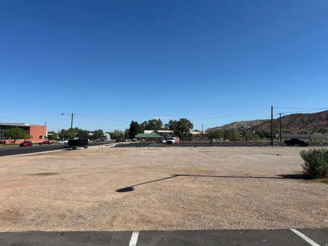 Expansive gravel lot with paved road frontage, utility poles, and distant hillside terrain