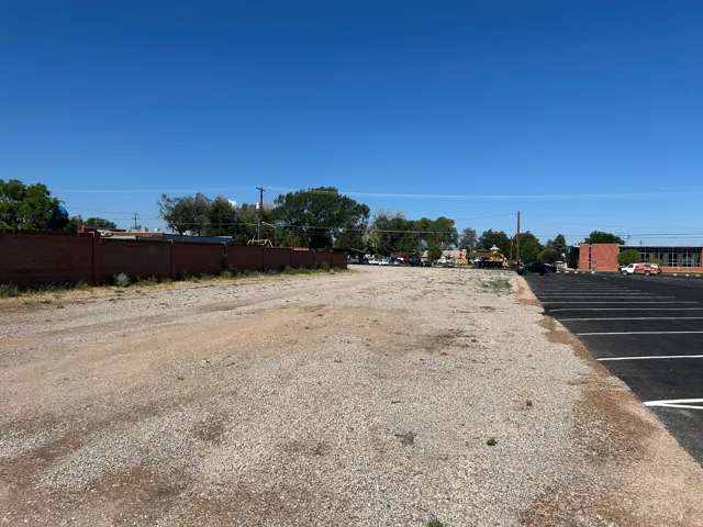 Expansive gravel lot featuring an adjacent paved parking area, a brick privacy wall, and mature perimeter trees