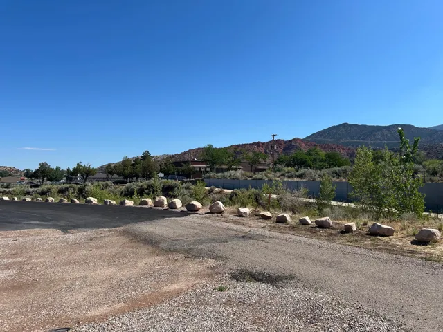 Expansive gravel and asphalt parking area with natural rock border, set against a backdrop of distant red-hued mountains