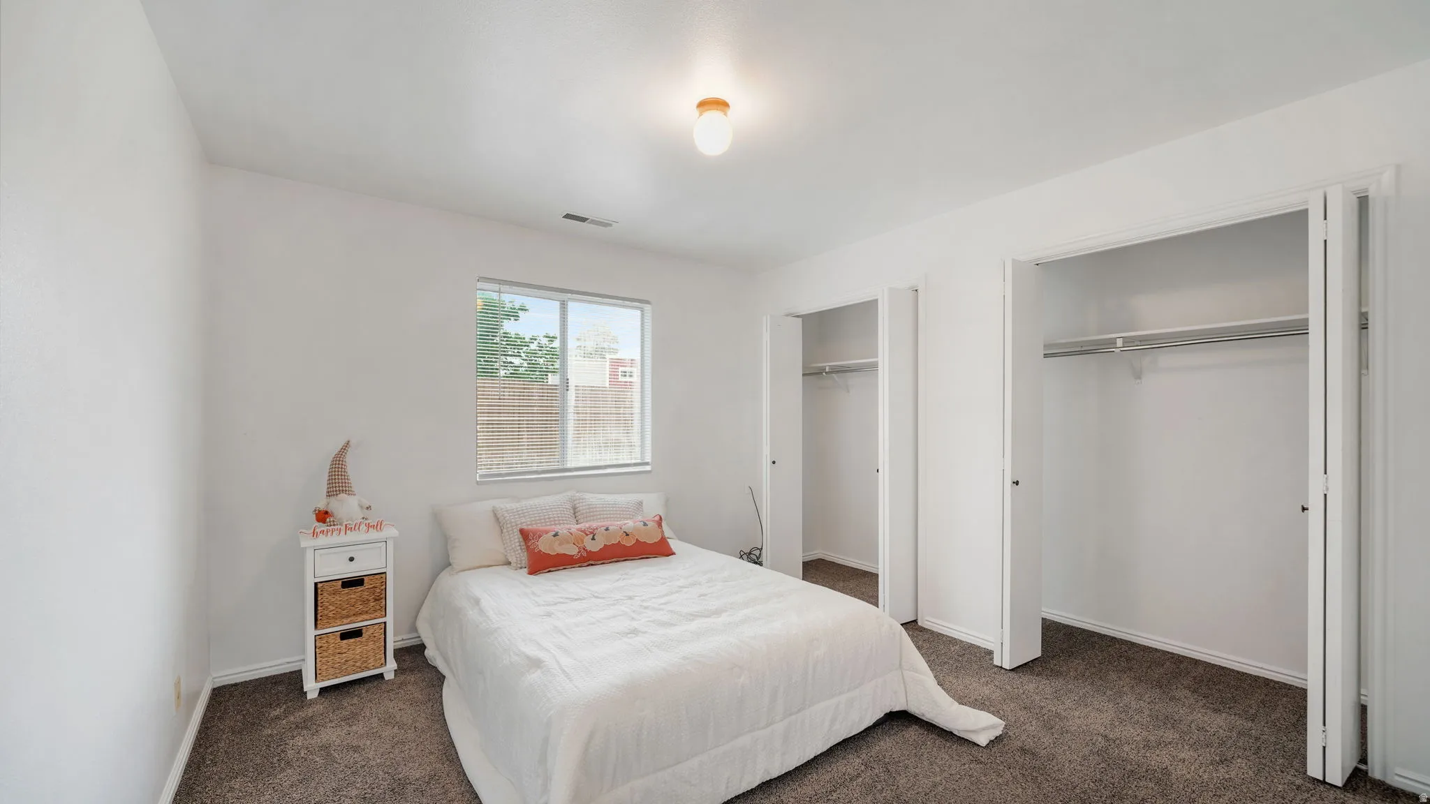Bedroom #2: Carpeted room featuring a single window with blinds, two bi-fold closet doors, and a ceiling-mounted light fixture