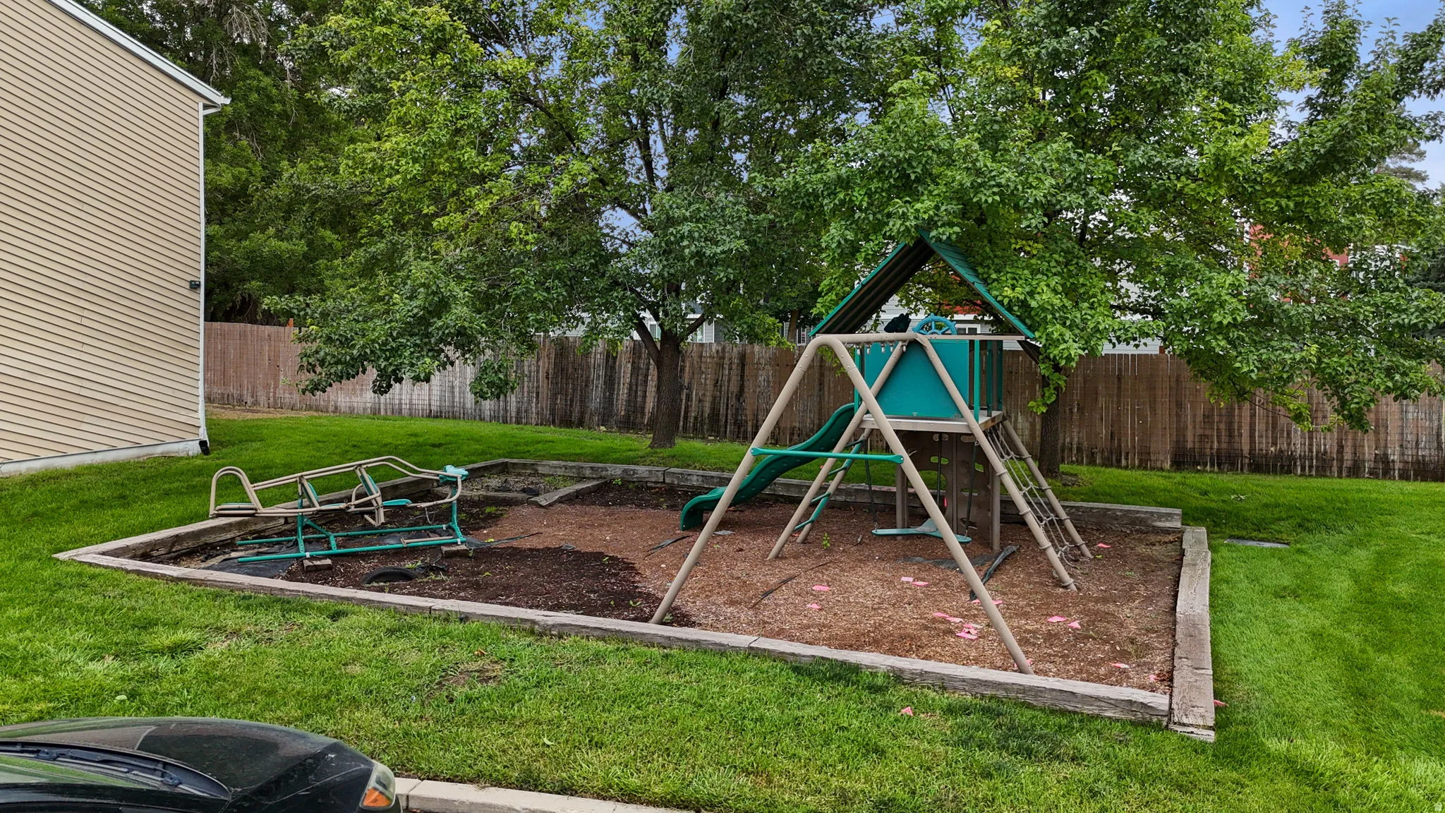 Outdoor play area with a swing set, slide, a separate play plane  and a wood-chip ground covering surrounded by a timber border