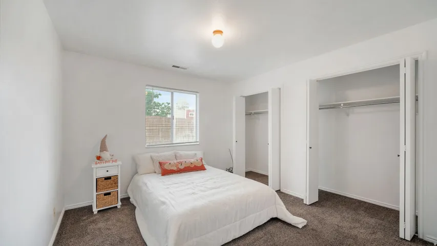 Bedroom #2: Carpeted room featuring a single window with blinds, two bi-fold closet doors, and a ceiling-mounted light fixture