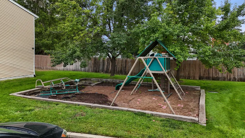 Outdoor play area with a swing set, slide, a separate play plane  and a wood-chip ground covering surrounded by a timber border
