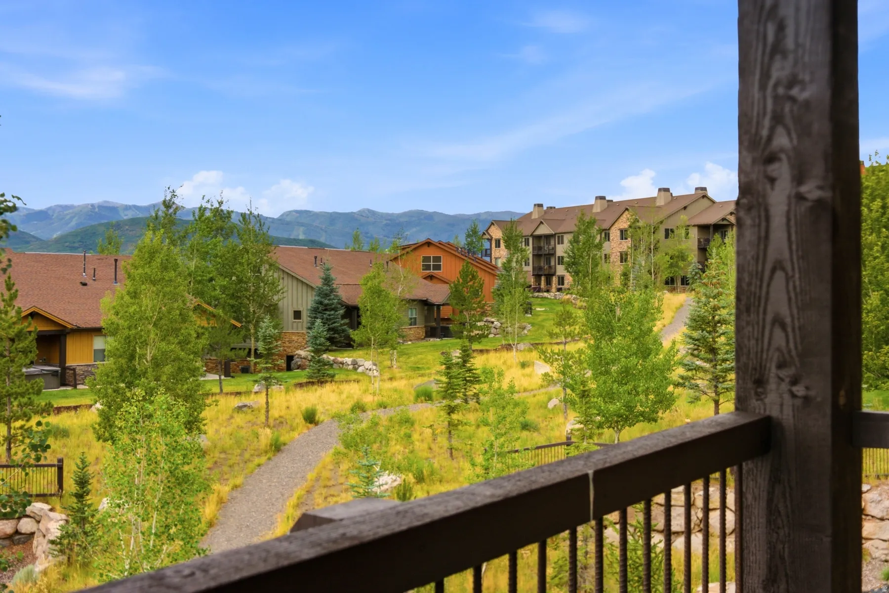 Outdoor balcony featuring a wood railing and post, overlooking a natural landscape with mature trees and distant mountains