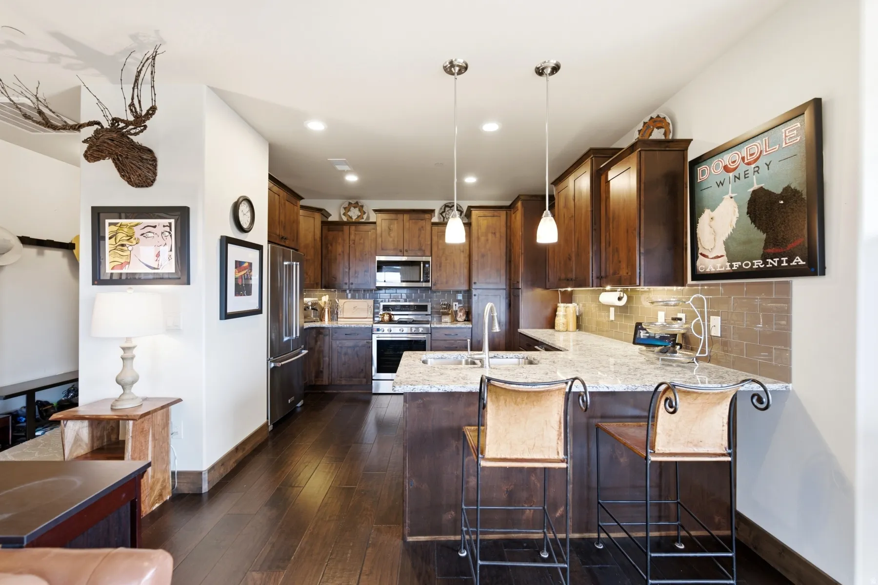 Kitchen featuring rich wood-finish cabinetry and flooring, stainless steel appliances, a tile backsplash, a large island with a stone countertop, and pendant lighting
