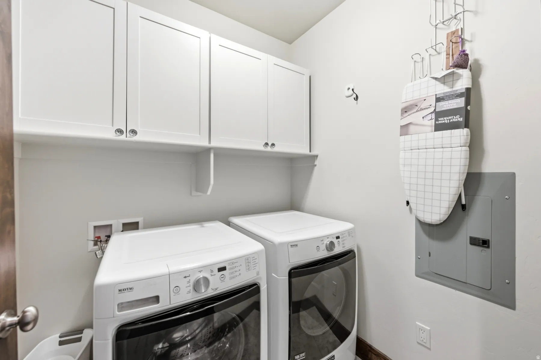 Dedicated laundry area featuring white shaker-style upper cabinetry, a coordinating white wall shelf, and light-toned wall paint