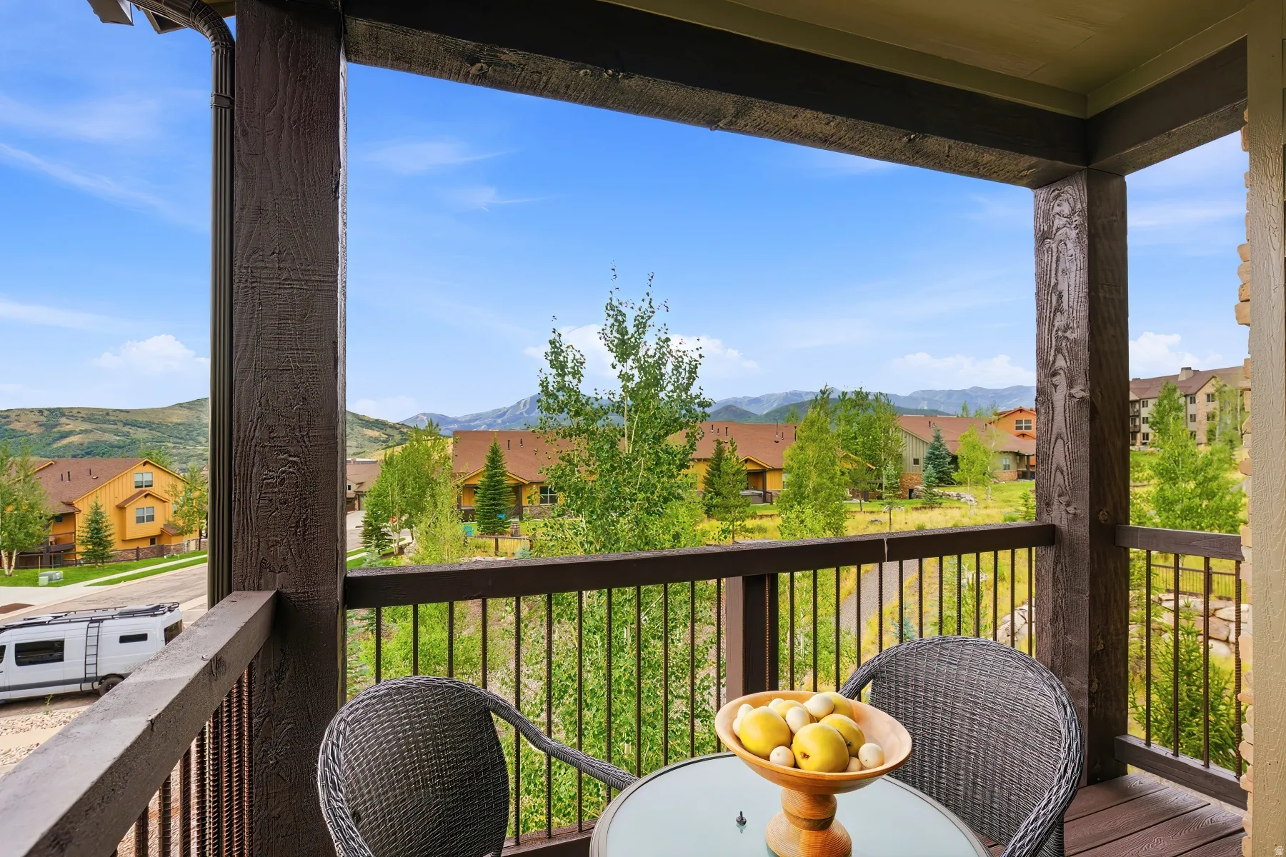 Covered balcony with wood-finish decking and railing overlooking a landscaped community and distant mountains