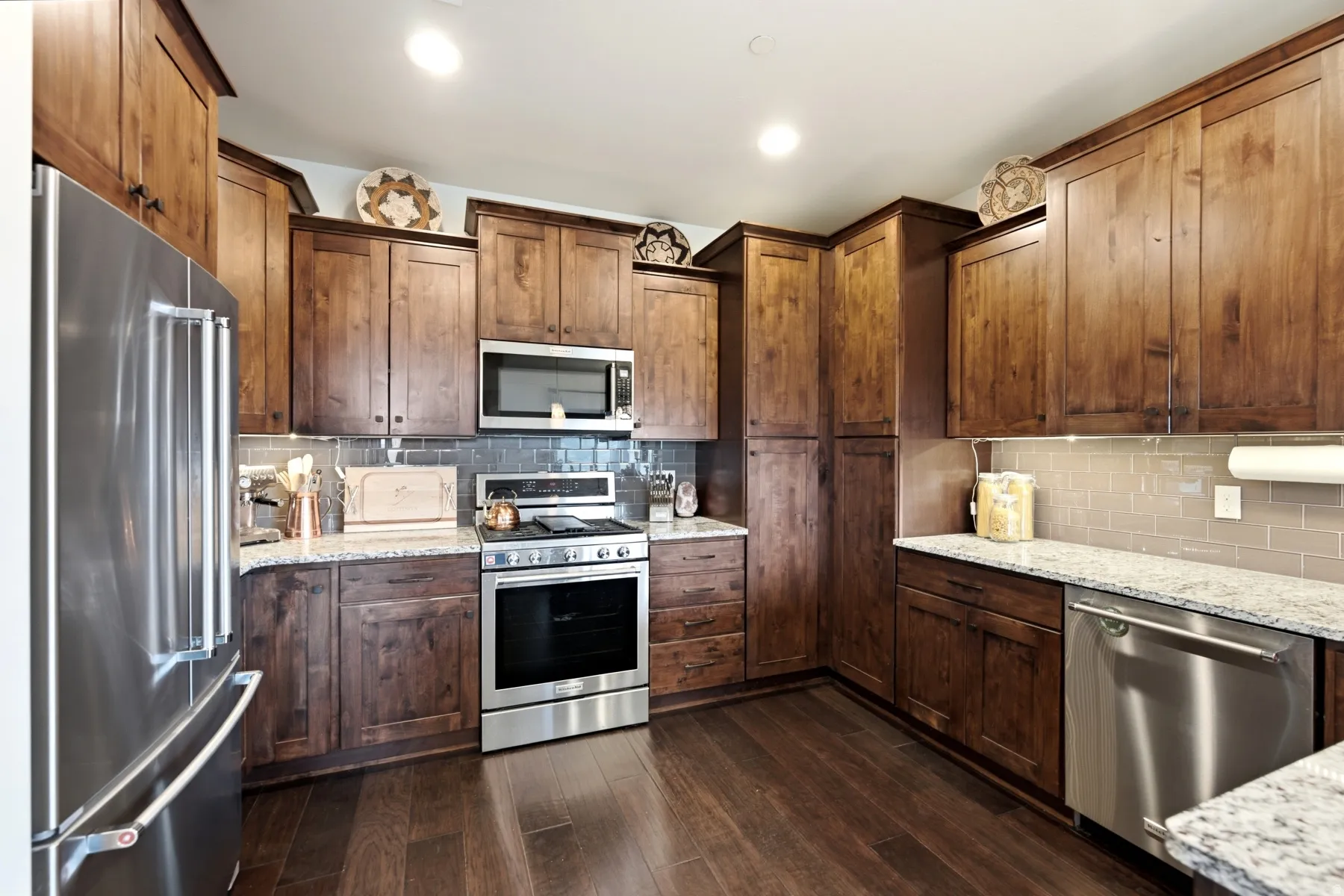 Kitchen featuring extensive wood cabinetry, stainless steel appliances, speckled stone countertops, a tile backsplash, and wood-finish flooring
