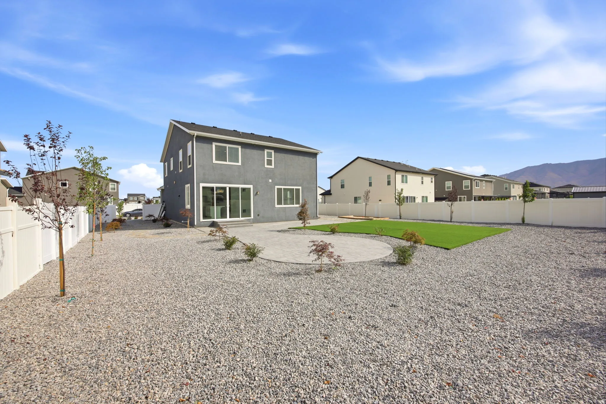 Expansive backyard featuring a gravel landscape, a circular paved patio, and a rectangular artificial turf area