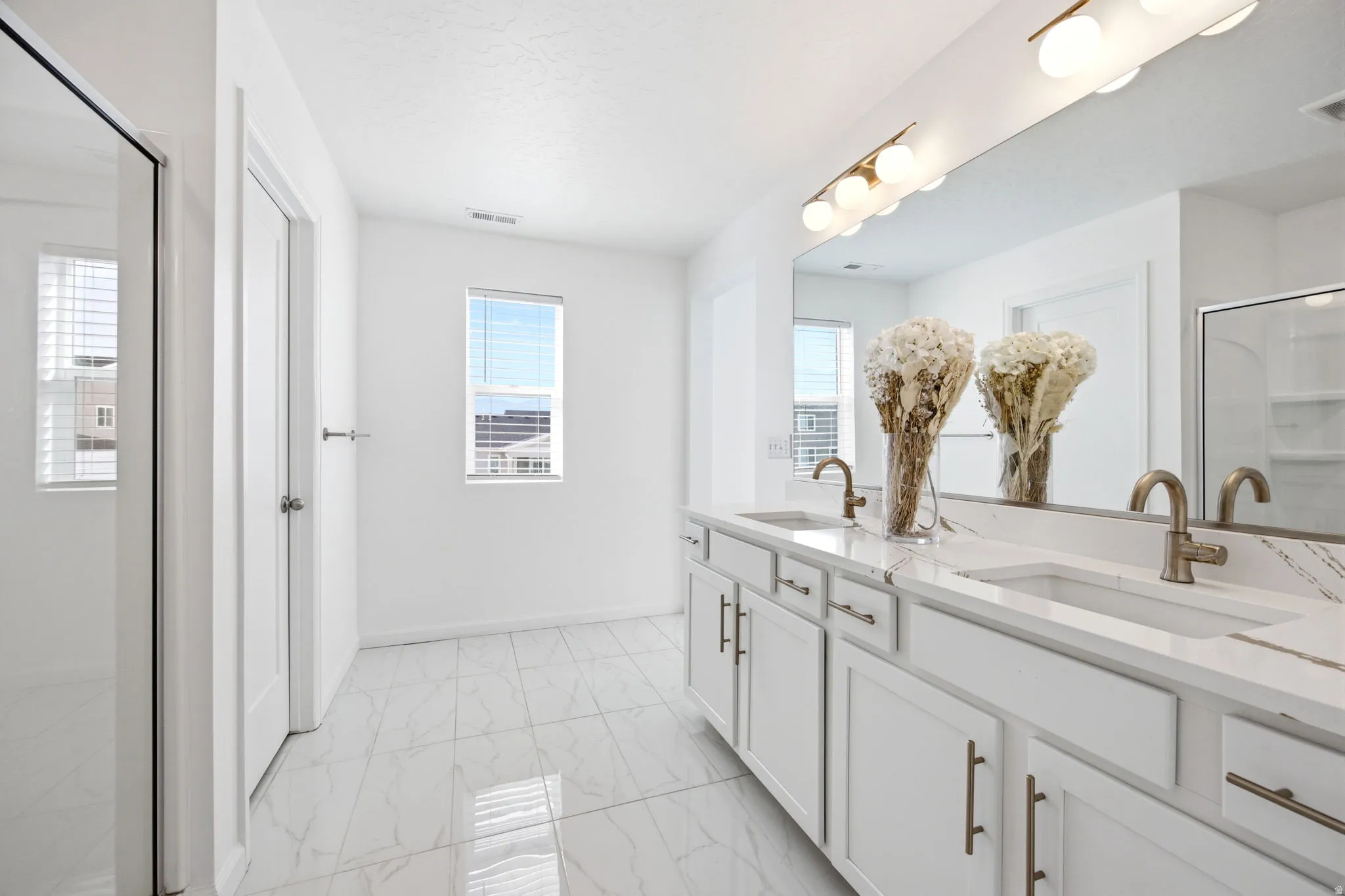 Spacious bathroom featuring a dual vanity with white cabinetry and light-toned countertops, two undermount sinks with brushed nickel fixtures, and a large mirror with contemporary globe lighting