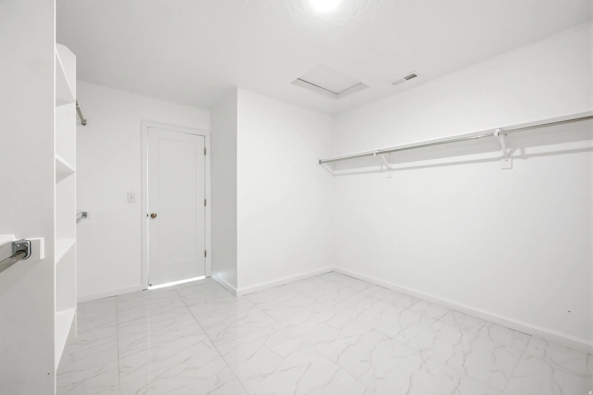 Spacious walk-in closet featuring white walls, white-finish built-in shelving, and white-finish hanging rods