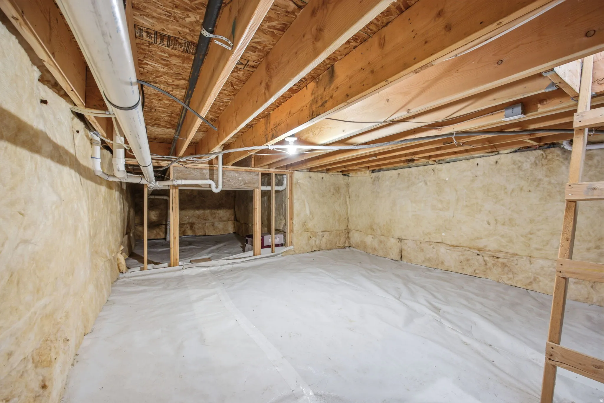 Unfinished lower level featuring exposed wood joists and subflooring, insulated walls, and visible plumbing and electrical infrastructure