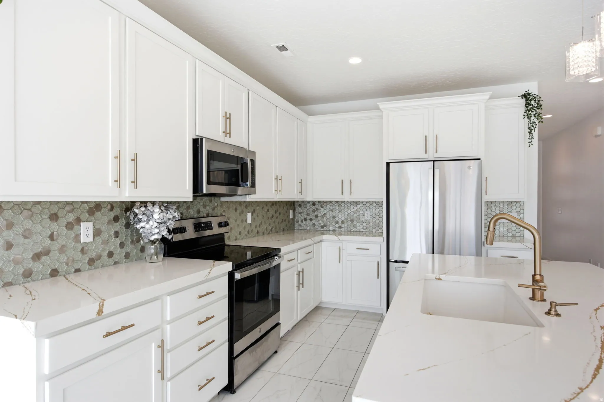 Contemporary kitchen featuring white cabinetry with gold-finish hardware, stainless steel appliances, and a hexagonal tile backsplash