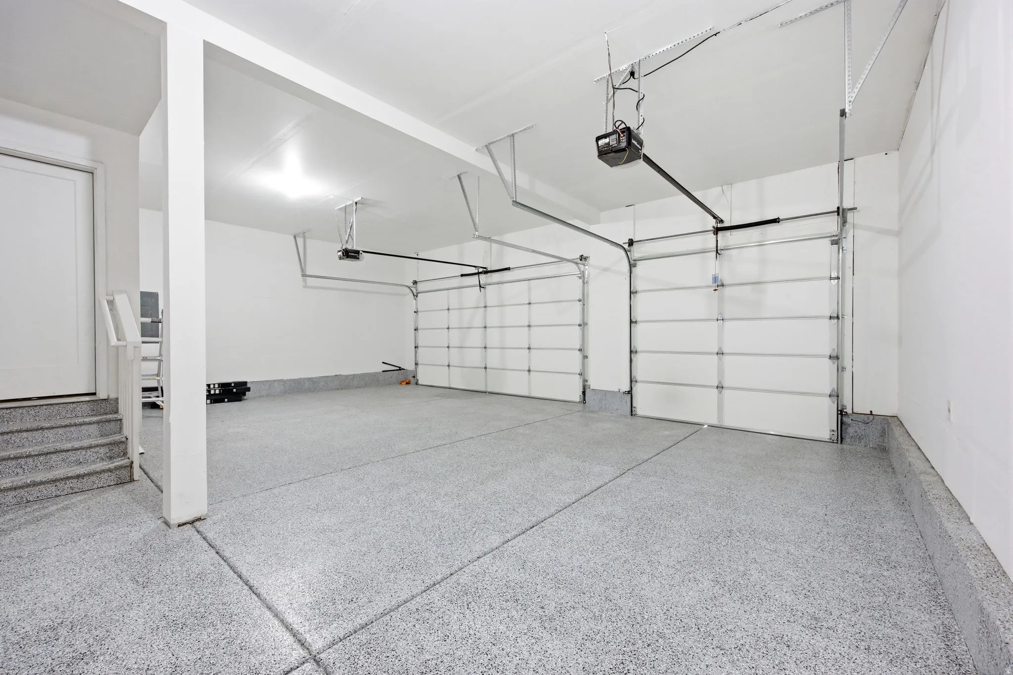 Two-car garage featuring a speckled epoxy floor coating, two overhead garage doors with automatic openers, and direct interior access via a white door and steps
