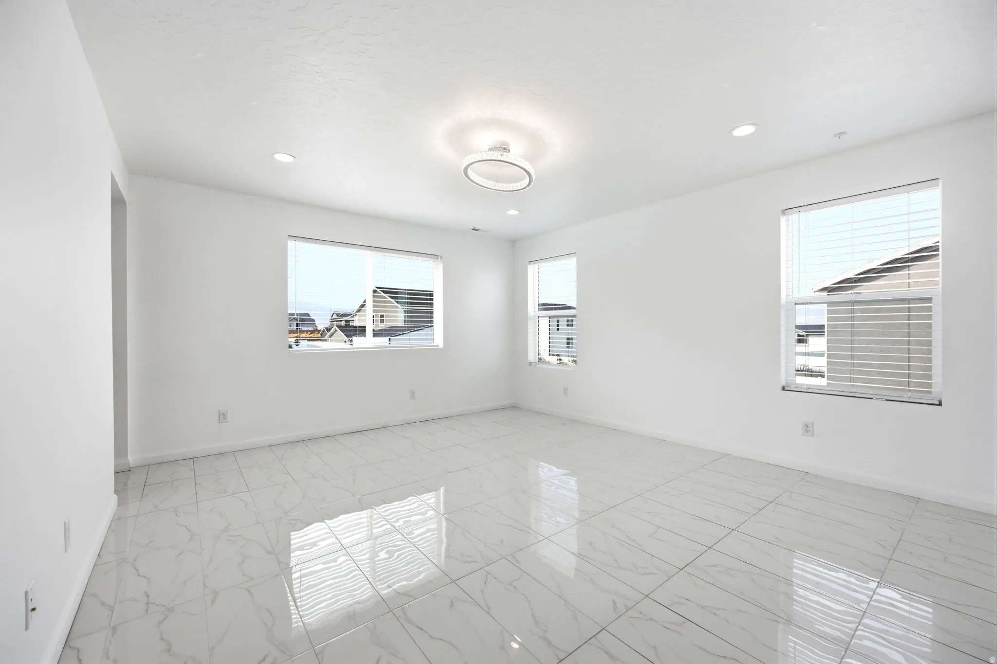 Bright room featuring large format white tile flooring with grey veining, three windows with horizontal blinds, a modern ceiling light fixture, and recessed lighting