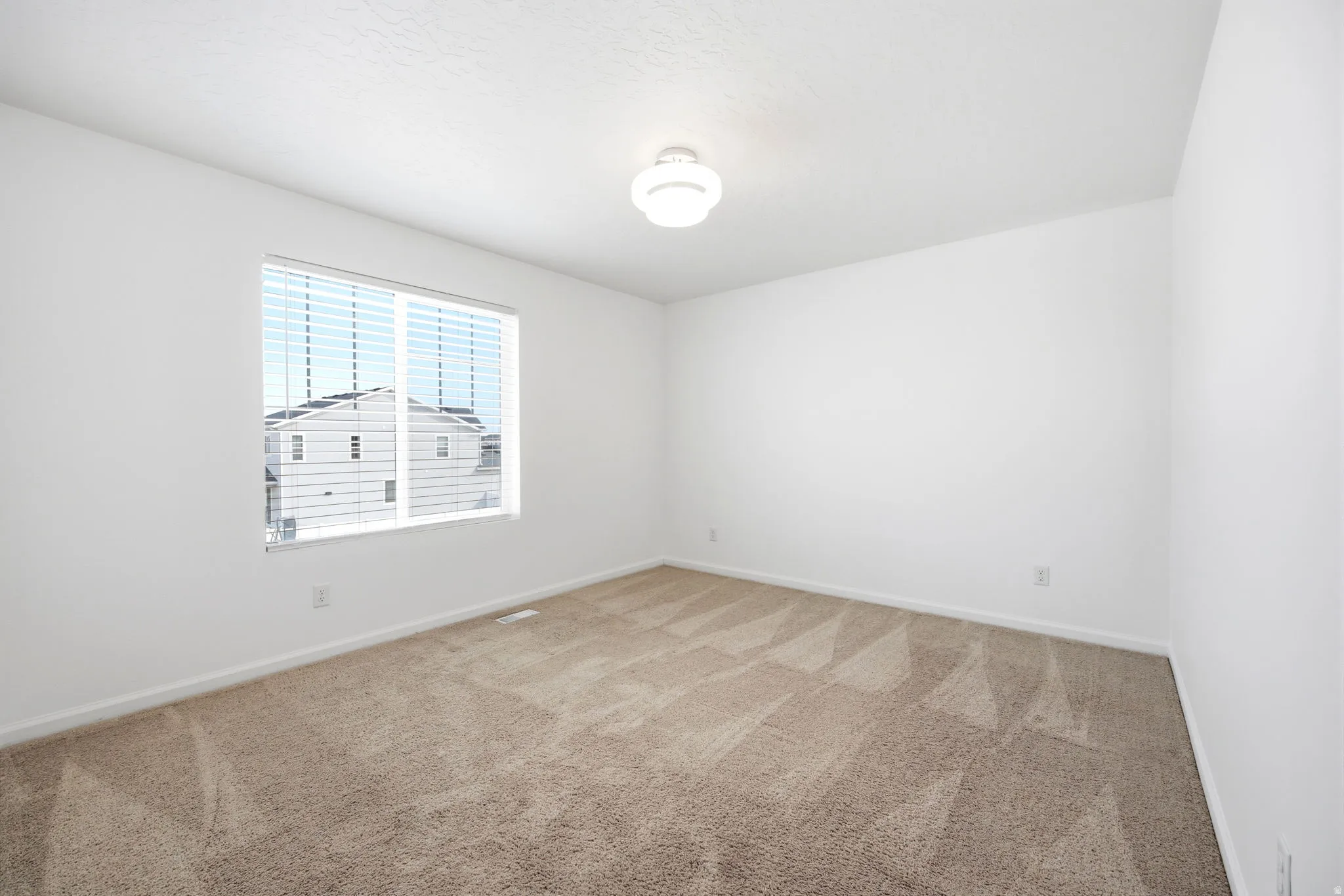 Bright room featuring a window with horizontal blinds, neutral wall paint, and textured carpeting